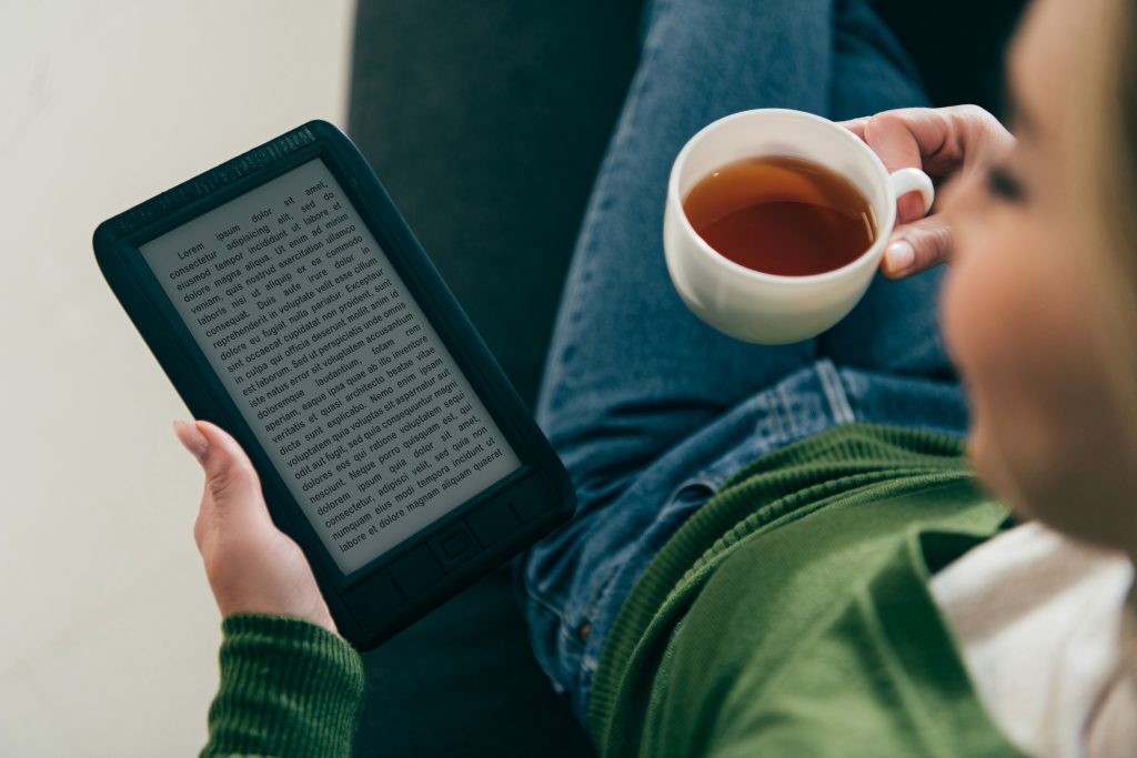 Smiling lady holding a warm cup of tea and reading on her tablet.